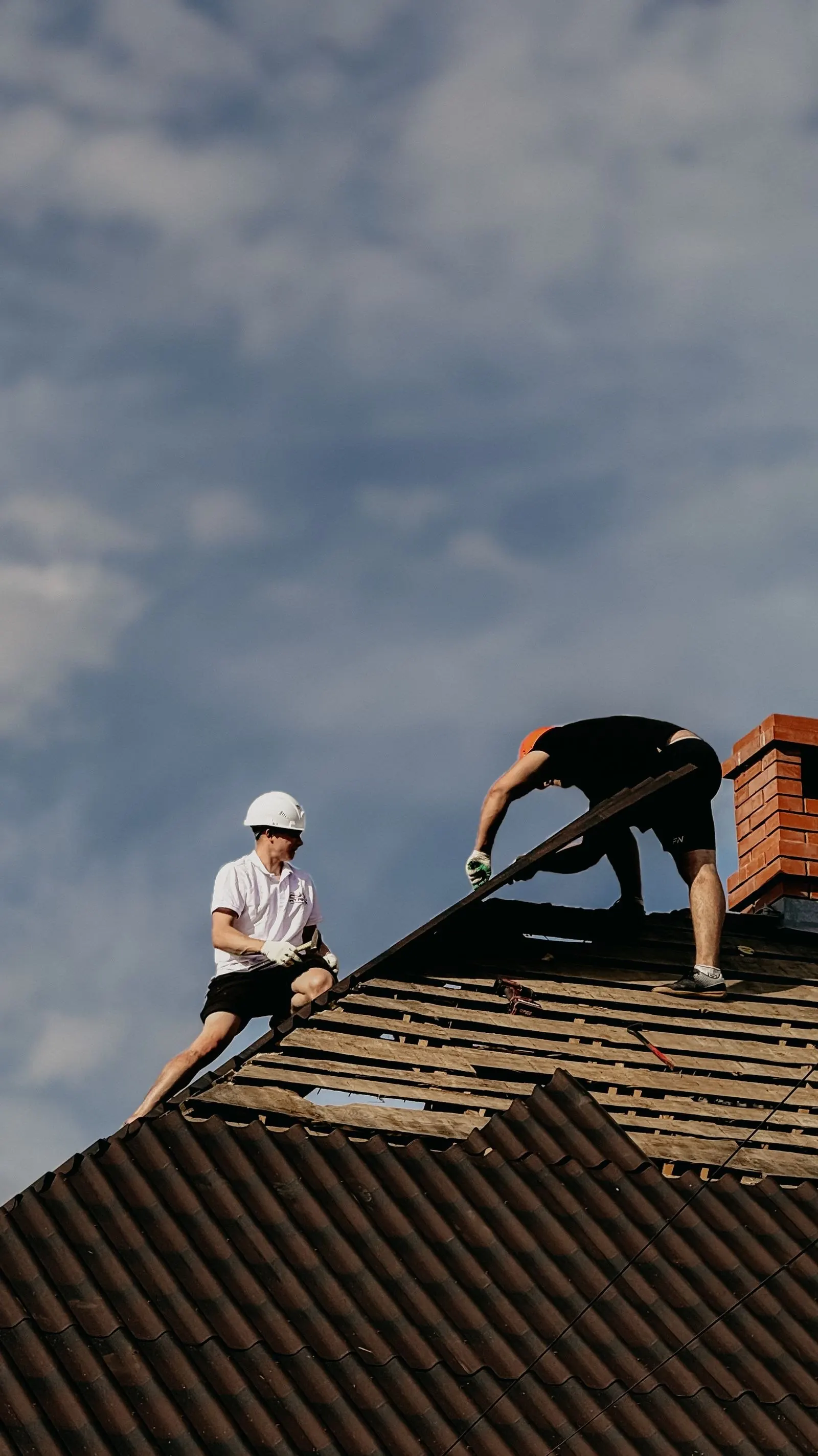 Roofers working on a shingle roof under a cloudy sky