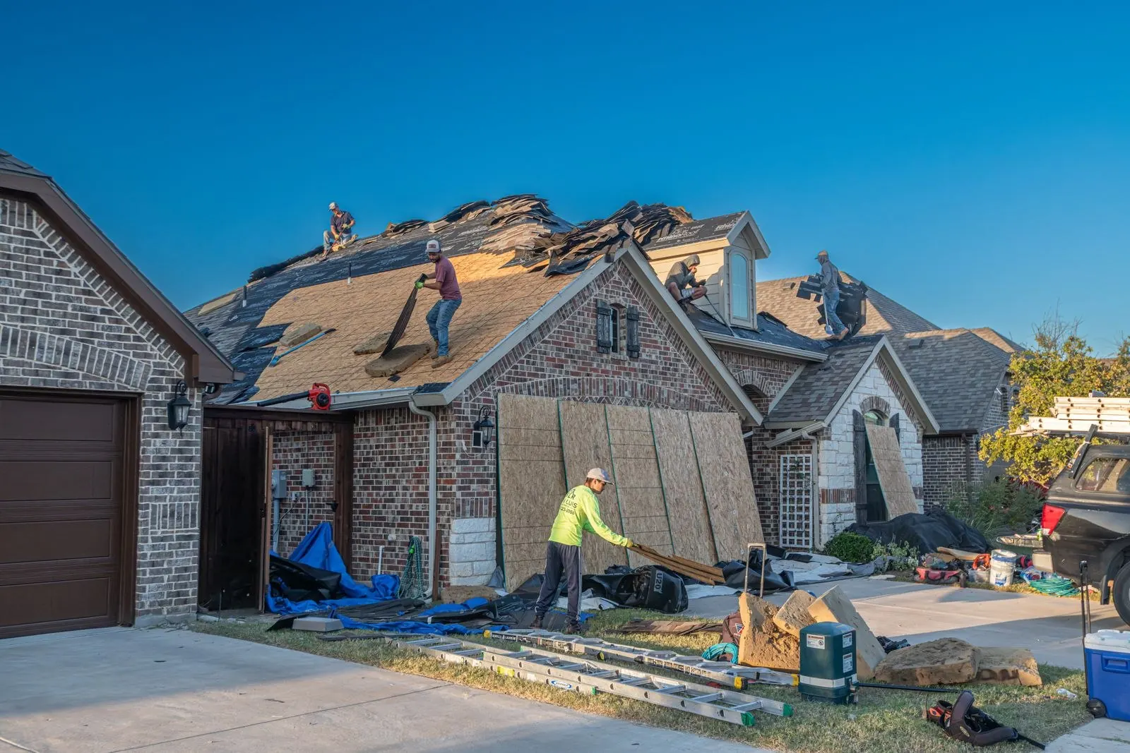 Roofers working on the shingles of a brick home